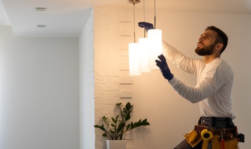 Electrician installing a modern light fixture in a residential setting, demonstrating professional electrical services