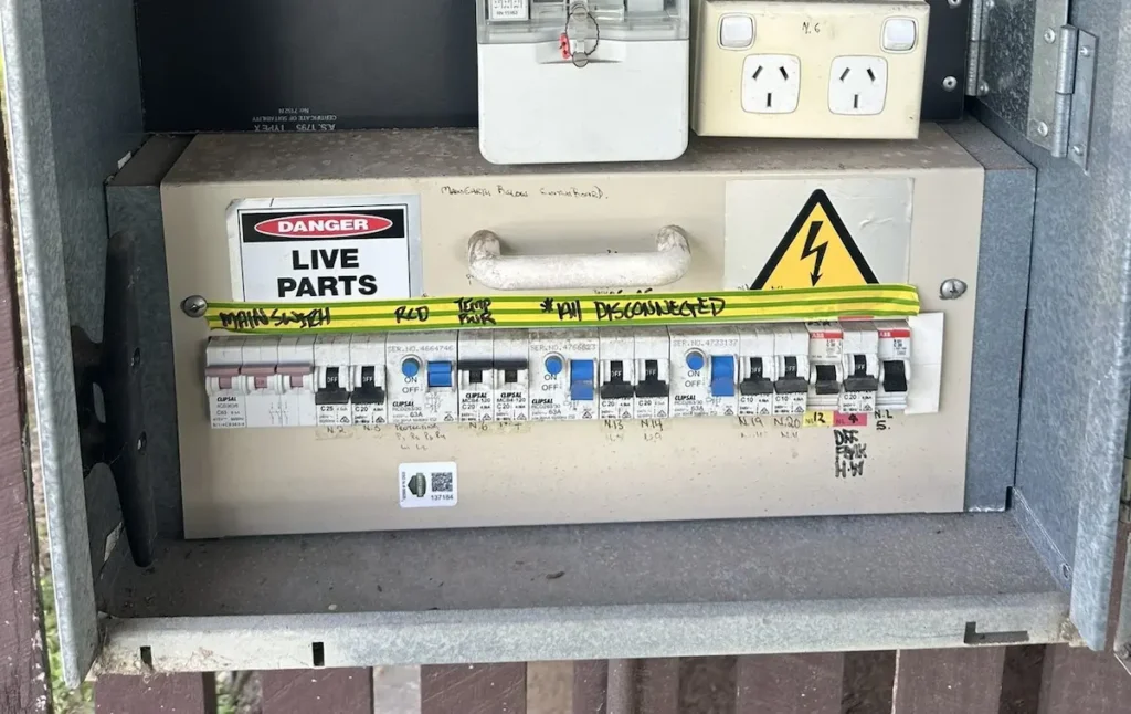 Old Tpanel meter board on Brisbane home with three round analogue meters Danger Live Parts warning sticker and ceramic fuses before SEQ Sparky full switchboard upgrade